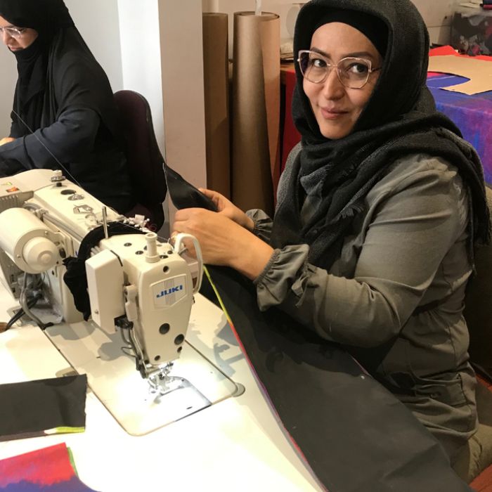 woman with glasses and headscarf smiling at camera while sitting at industrial sewing machine learning to sew