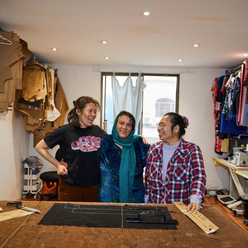 3 women standing at a cutting table smiling at each other
