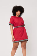 woman with curly hair in red dress cinched with red and white elastic belt stands with her arms at her side against a white backdrop