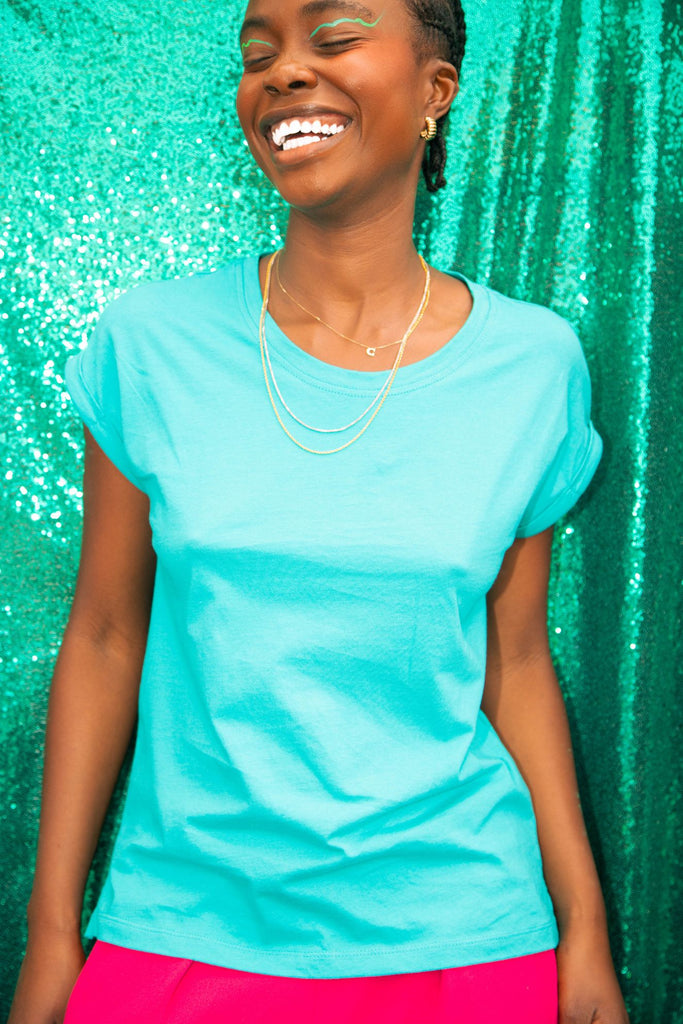 turquoise coloured dorsu rolled sleeve top with pink pants against green sequin backdrop