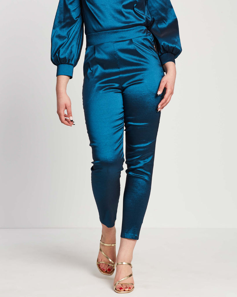 woman wearing shimmery teal straight leg pants with matching bishop sleeve top tucked in to waistband and gold strap heels