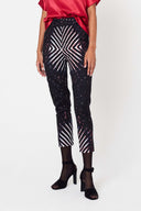 person standing with arms by their side wearing a pink shiny top and printed black straight leg pants with black heels and stockings against a white backdrop