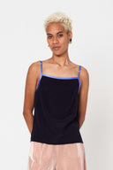 person with short blonde hair wearing purple bind silk camisole with light pink wide pants against white backdrop