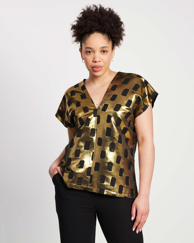 woman wearing shiny gold karen top with black rectangle pattern on top of black straight leg pants