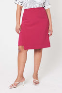 woman with hands by her side standing wearing white top with pink wrap skirt against white backdrop