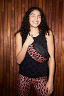 woman with curly hair smiling wearing a cross-body bum bag against a wooden back drop