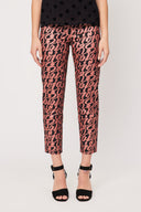 womans legs wearing a pair of black pants with a copper curl print, black heeled sandals and a black sheer blouse with her arms at her side against a white backdrop