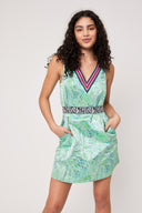 woman with curly hair wearing a green dress cinched with a zebra pattern elastic belt stands with both hands in the pocket of the dress against a white backdrop.