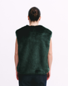 Person wearing a dark green fur vest on a white background