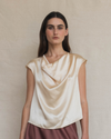 Woman wearing a beige sleeveless top against a plain background