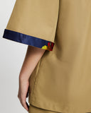 Close-up of a person wearing a tan Quarter Sleeve Trench with Nour community print band at the hem of sleeve