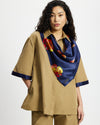 Woman wearing a Tan Short Quarter Sleeve Trench and shorts set with navy trim on a white background and matching Nour Square Scarf around her neck