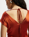 Back view of a person wearing an orange dress with a tie detail on a plain background