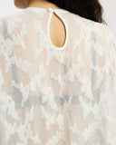 Model wearing white sheer oversized top with keyhole details