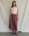 Woman wearing a cream top and maroon skirt against a plain background