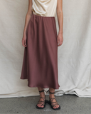 Person wearing a burgundy skirt and beige top against a plain background