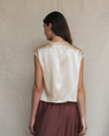 Woman wearing a cream top and brown skirt against a plain background