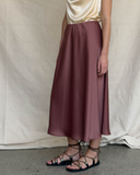 Person wearing a maroon skirt and black sandals against a neutral background