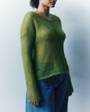 Person wearing a green sweater and blue jeans against a plain background
