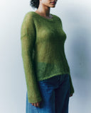 Person wearing a green sweater and blue jeans against a plain background
