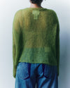 Person wearing a green sweater and blue jeans against a plain background