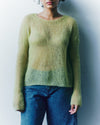Person wearing a green sweater and blue jeans against a plain background