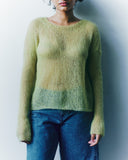 Person wearing a green sweater and blue jeans against a plain background