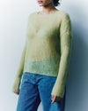 Person wearing a green sweater and blue jeans against a plain background