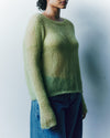 Person wearing a green sweater and blue jeans against a plain background