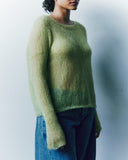 Person wearing a green sweater and blue jeans against a plain background