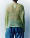 Person wearing a green sweater and blue jeans against a white background