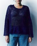 Person wearing a dark blue sweater over a sheer top with light blue jeans against a plain background