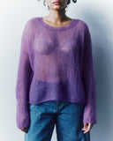 Person wearing a purple sweater and blue jeans against a plain background