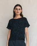 Woman wearing a dark floral patterned top against a plain background