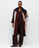 Person wearing a long, multi-colored coat over a dark outfit on a white background