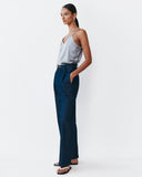 Woman wearing a silver tank top and navy pants on a white background