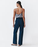 Woman wearing a silver top and navy pants on a white background