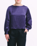Person wearing a purple satin top and black pants on a white background