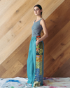Woman wearing a grey tank top and colorful patterned pants against a wooden wall.