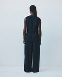 Person wearing a dark blue sleeveless top and wide-leg pants against a white background