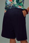 A person wearing black pleated shorts and a colourful floral print blouse, shown from the back against a plain light gray background.
