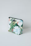 A small zippered pouch with a colorful floral and botanical print, featuring large white and light blue flowers with green leaves, set against a plain light gray background.