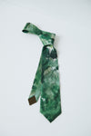 A green necktie with a marbled or watercolor-like pattern in various shades of green, black, and white, tied in a knot and displayed against a plain white background.