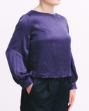 Person wearing a purple satin top with long sleeves on a white background