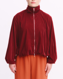 Person wearing a red velvet jacket and orange pants on a white background