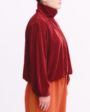 Person wearing a red velvet jacket and orange pants on a white background