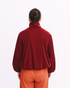 Person wearing a red velvet jacket and orange pants on a white background
