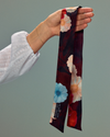 Model holding a burgundy floral twilly scarf.