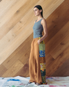 Woman wearing a sleeveless top and patchwork pants against a wooden wall.