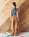 Woman wearing a sleeveless top and colorful pants standing against a wooden wall.